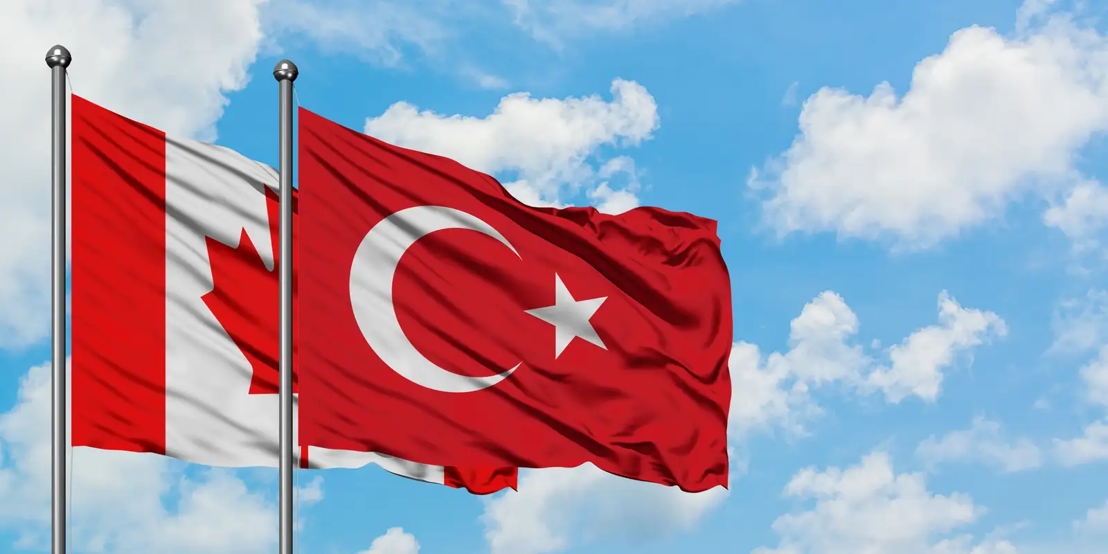Mavi gökyüzünde yan yana dalgalanan Kanada ve Türkiye bayrakları
